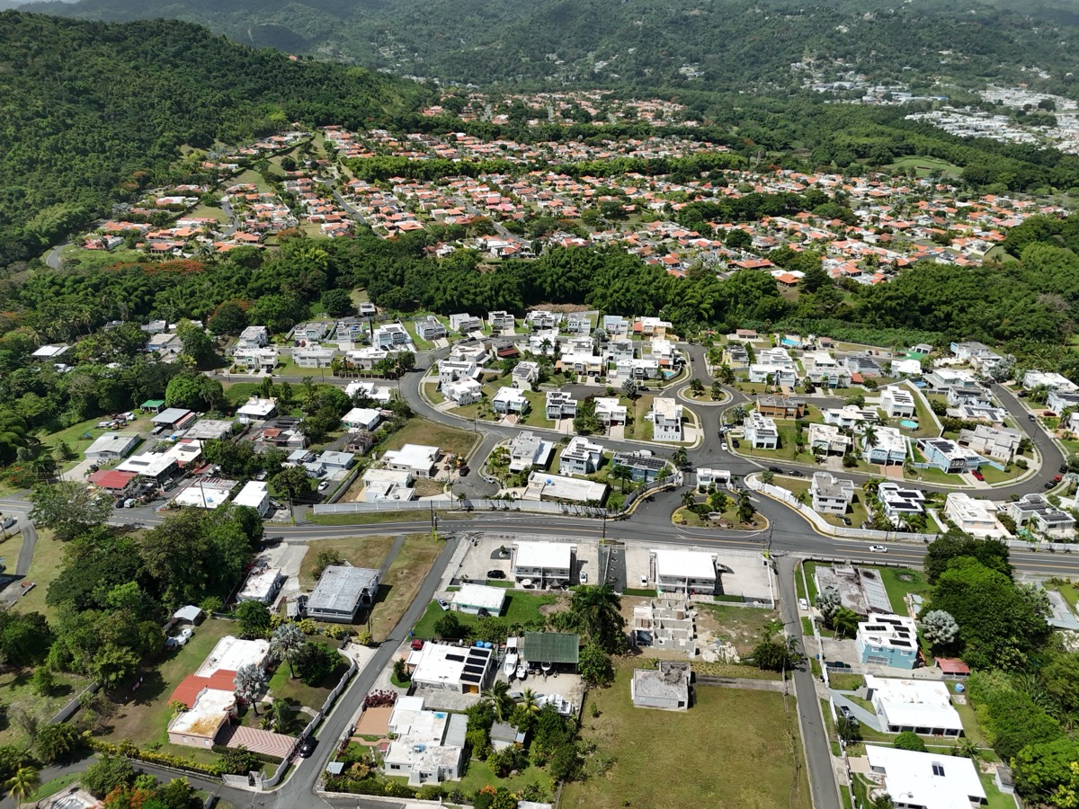Wide aerial overview of Puerto Rico neighborhood showing streets and homes nestled in green hills